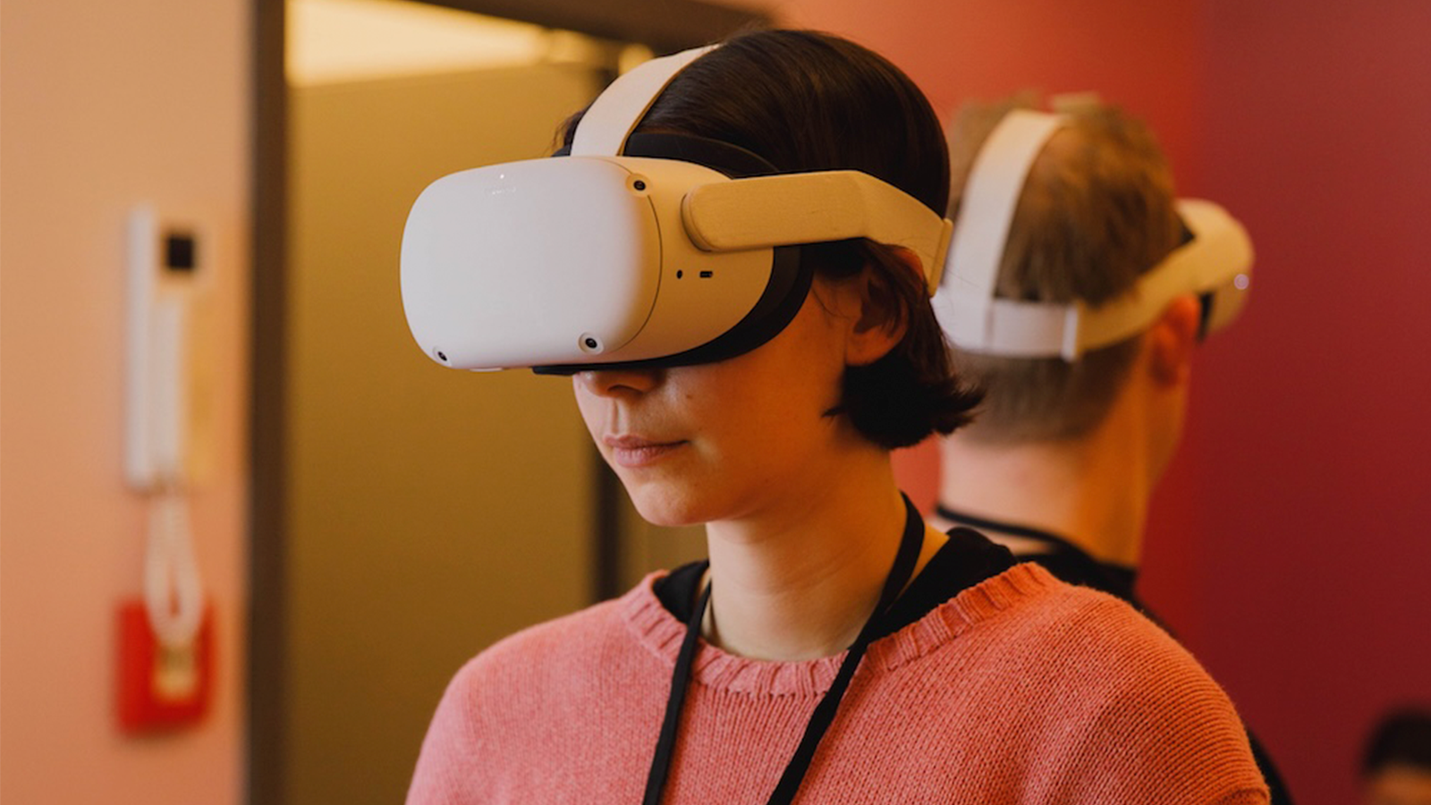 Eine junge, dunkelhaarige Frau in einem rosa Pullover testet eine VR Brille. nextMedia.Hamburg