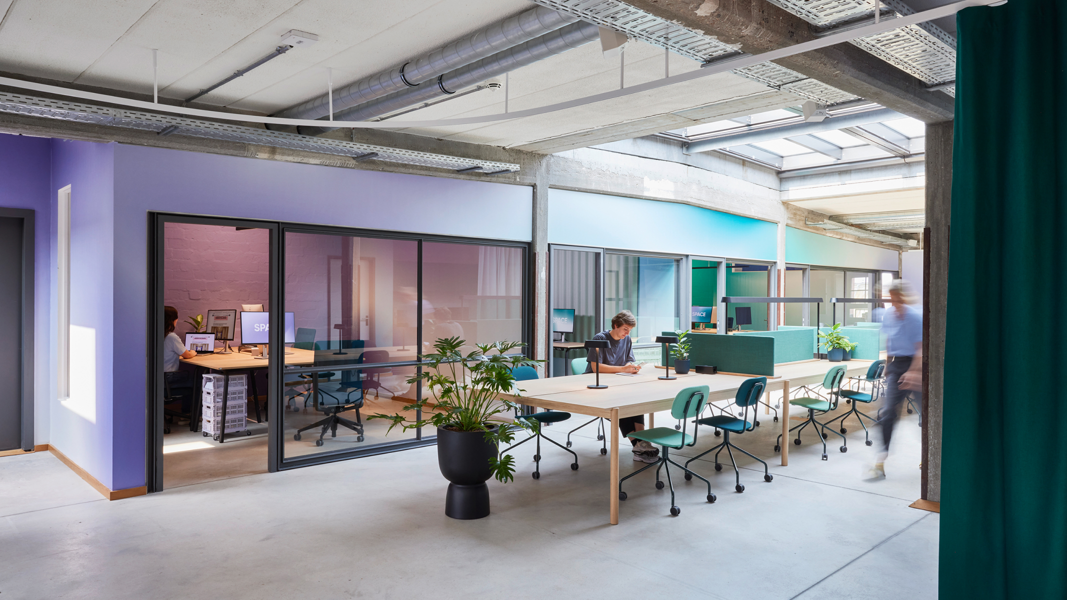 In a storage room there are two further rooms with purple walls and window fronts. In the centre of the room is a long table with workstations. nextMedia.Hamburg